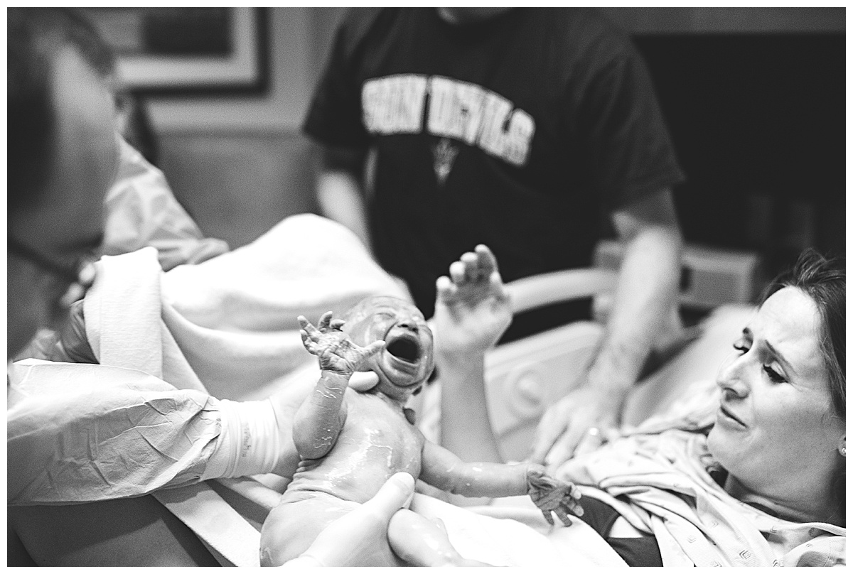 doctor handing crying newborn to happy mom after delivery