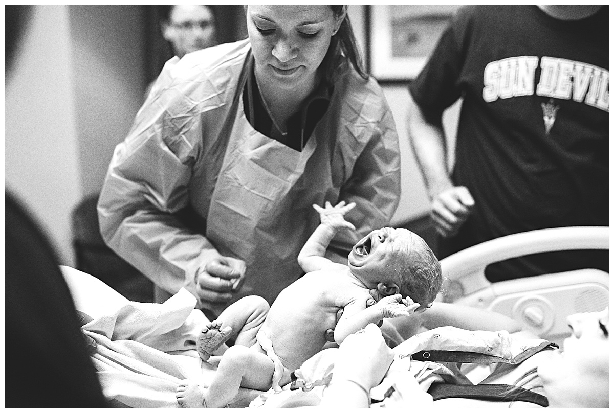 nurse helps hand newborn baby to mom in delivery room