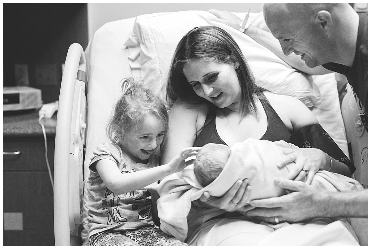 big sister grins at newborn baby brother in delivery room