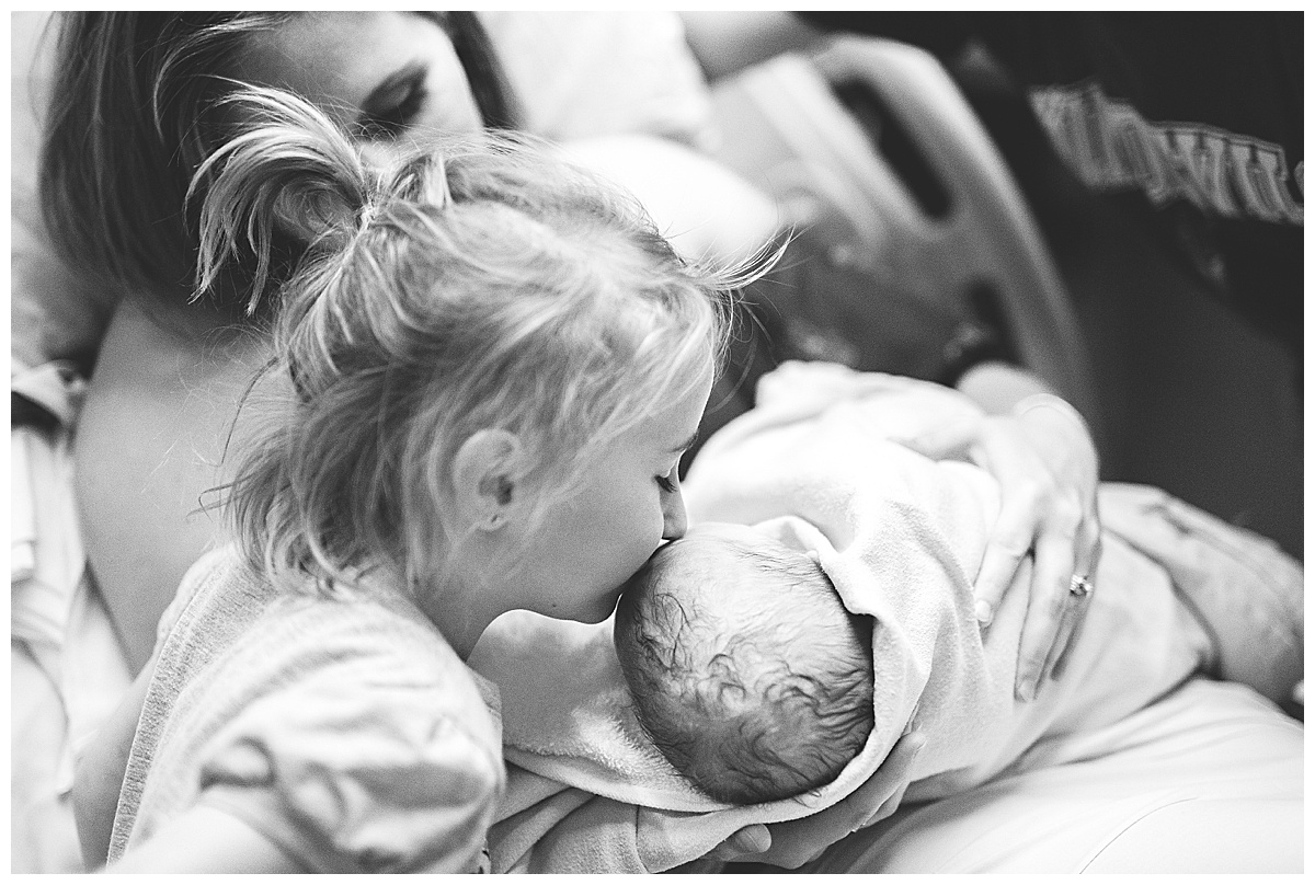big sister kisses brand new baby brother on head in delivery room