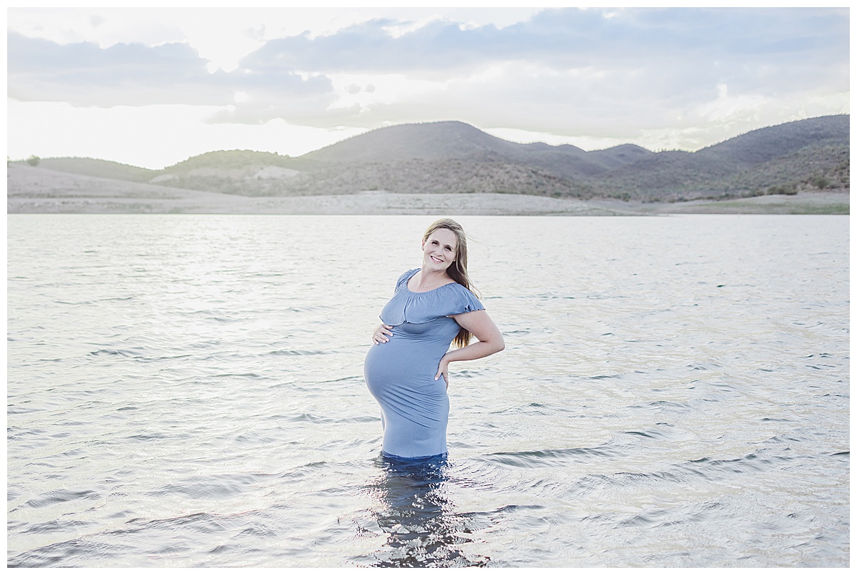 pregnant mom wearing dark blue dress standing in water at Lake Pleasant