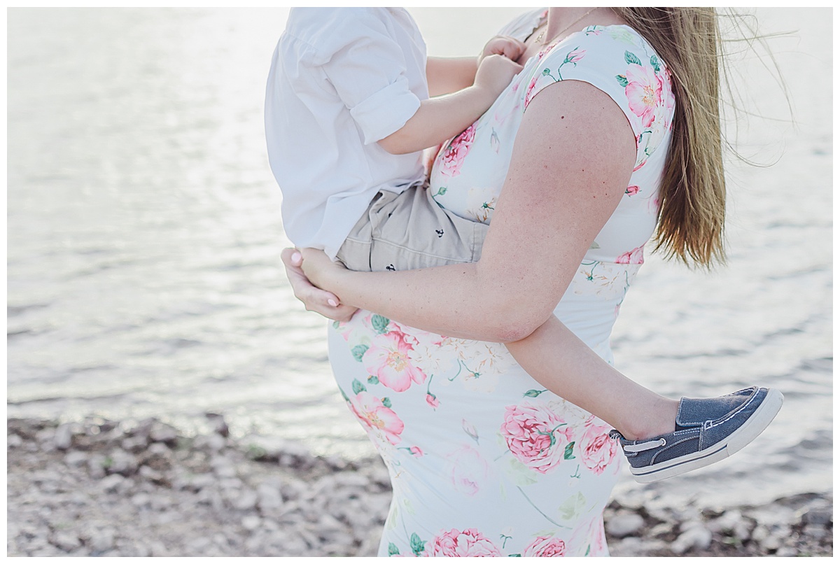 mom holding four year old son atop her pregnant belly during maternity photo session