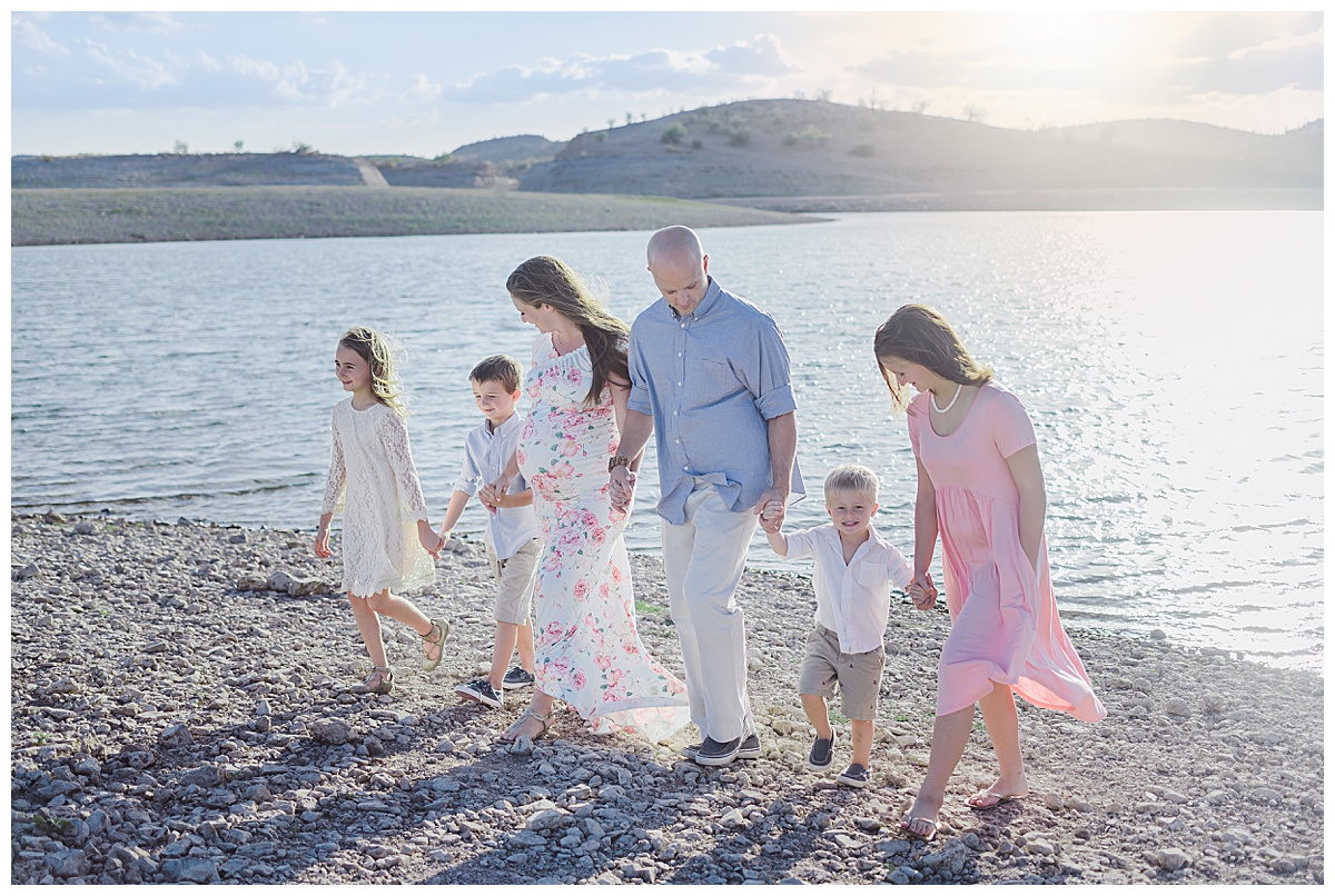 Family of six walks along the shore of lake pleasant during family maternity session
