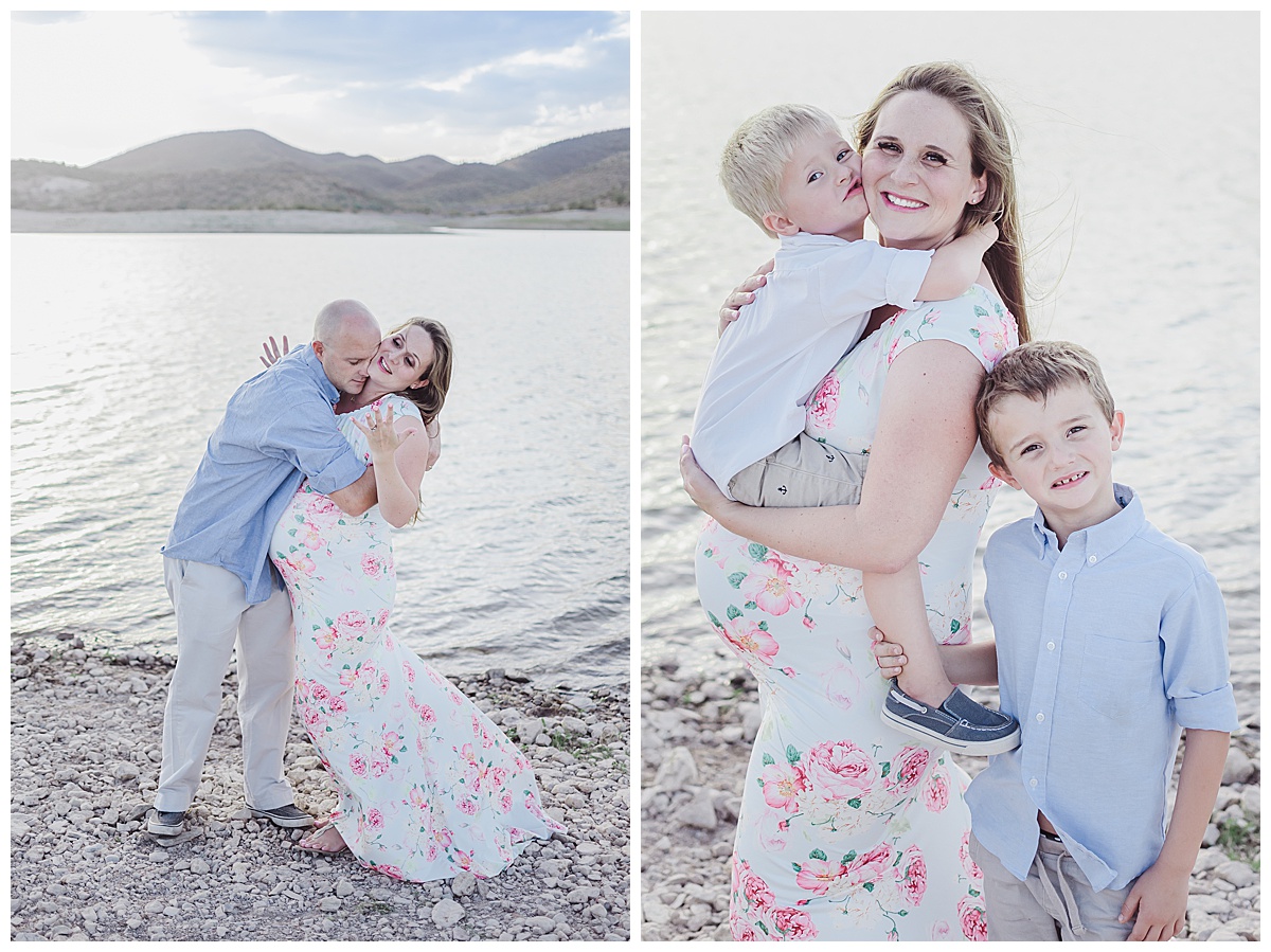 Pregnant woman in blue and pink floral dress poses with husband and her two boys during a maternity photo session at the lake