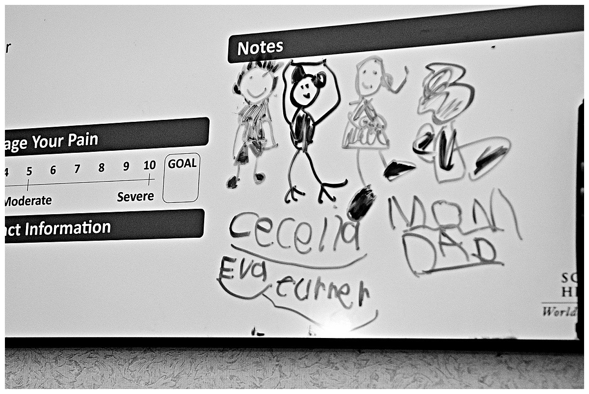 black and white image of hospital delivery room dry erase board with drawings done by a five year old of her new sibling