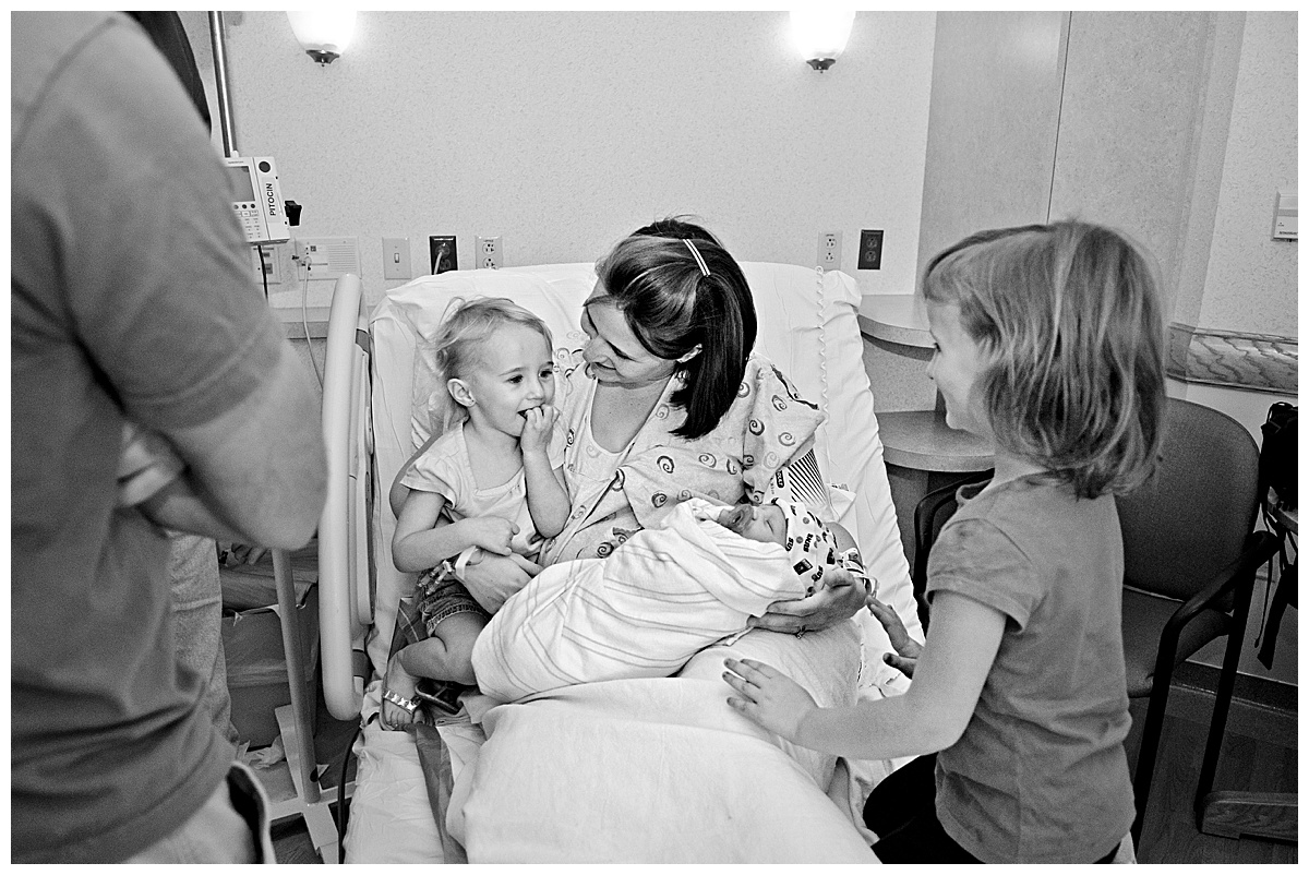black and white image of new big sister meeting her baby brother for the first time