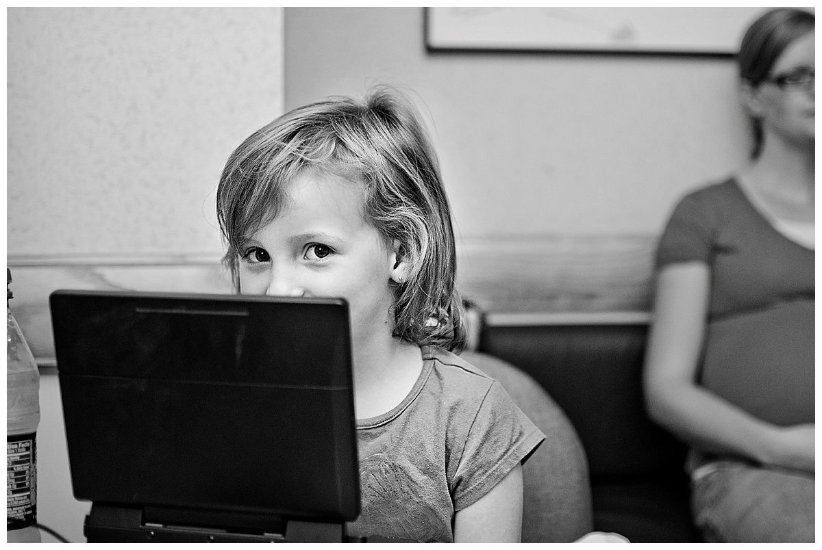 black and white image of little girl looking over the top of a computer screen while waiting for new baby to be born