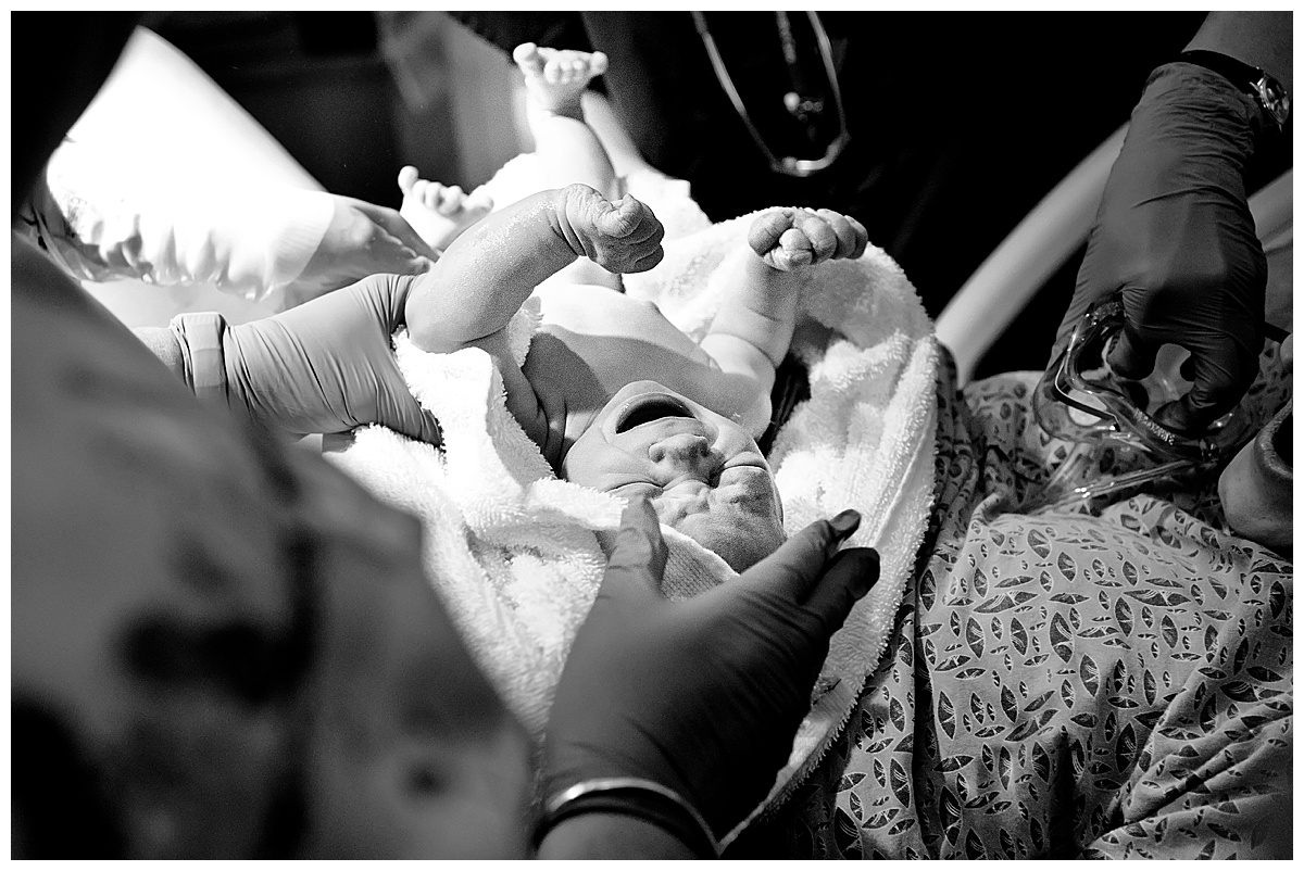 black and white image of newborn baby boy being placed on mom's stomach