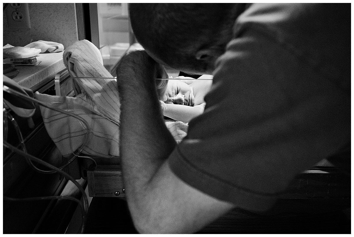 black and white image of dad looking at new baby in hospital delivery room