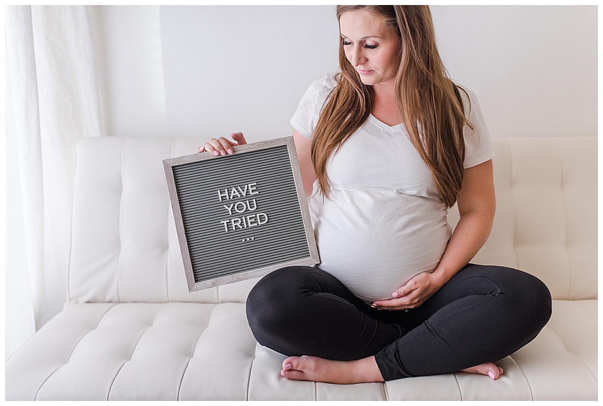 overdue pregnant woman sitting cross leg on a futon holding a letter board that says "Have you tried..."