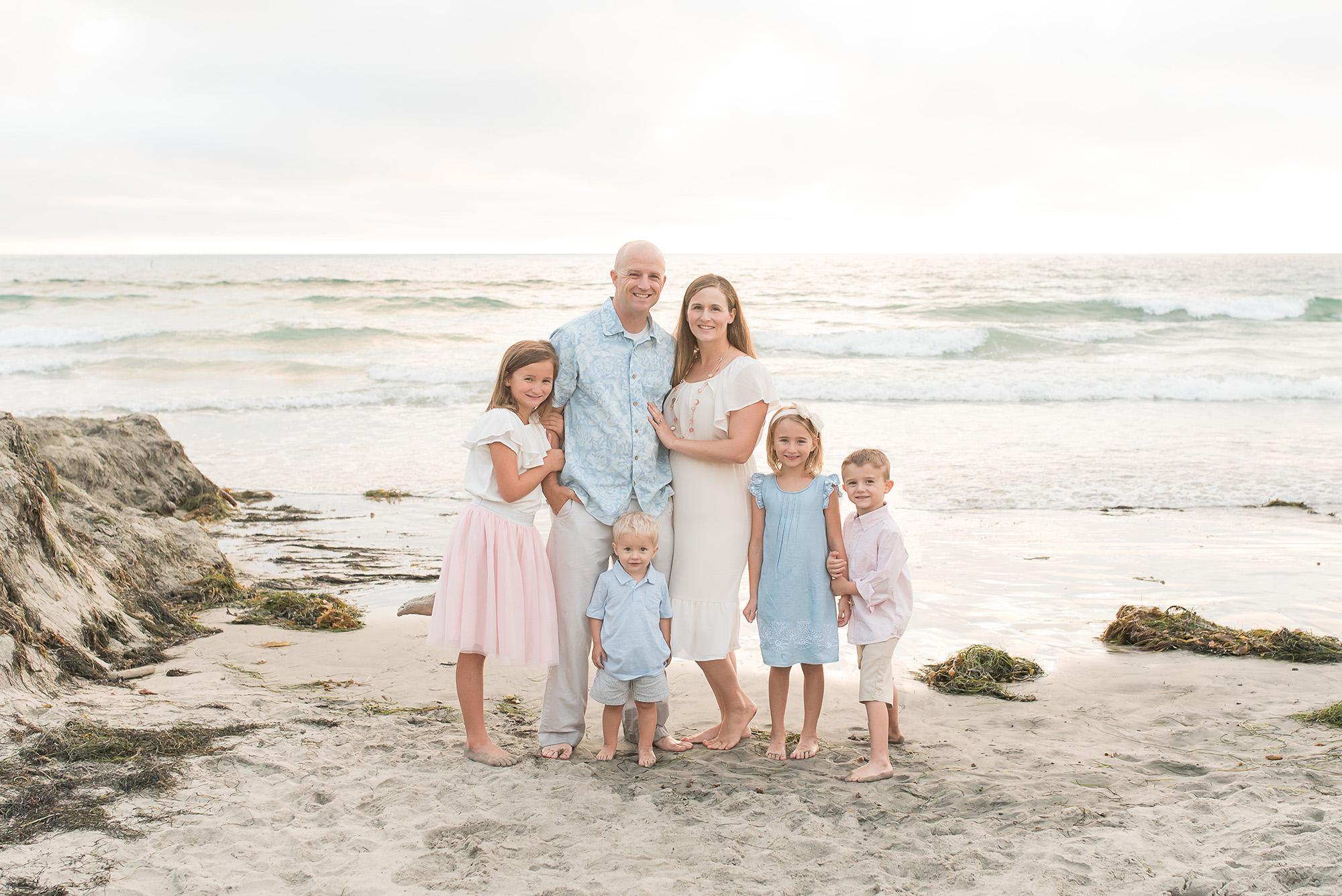 Family dressed in pink, cream and blue posing for a family portrait at La Jolla Beach, California